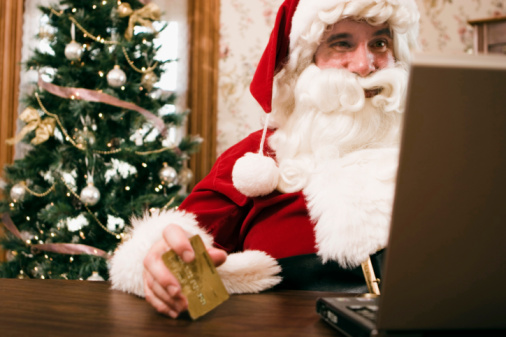 Santa Claus sitting in front of a laptop and holding a credit card