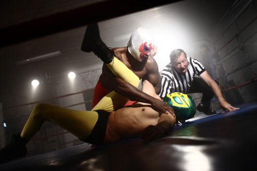 Referee watches as two masked wrestlers fight