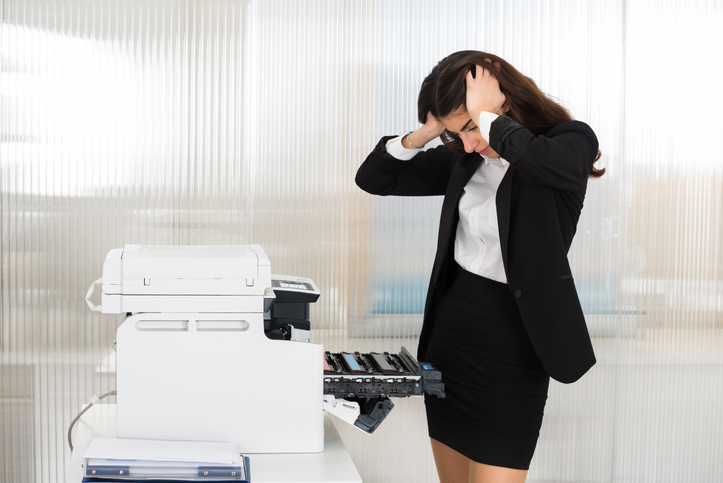 Irritated young businesswoman looking at printer machine at office